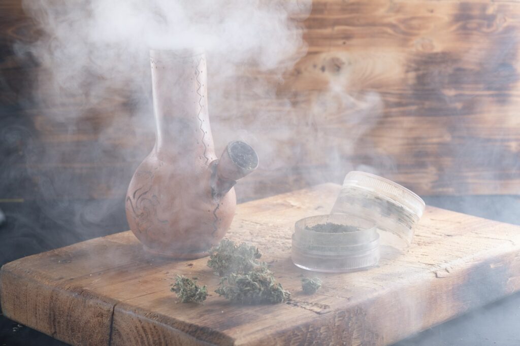 bong and open grinder cannabis and marijuana in smoke are located on the board