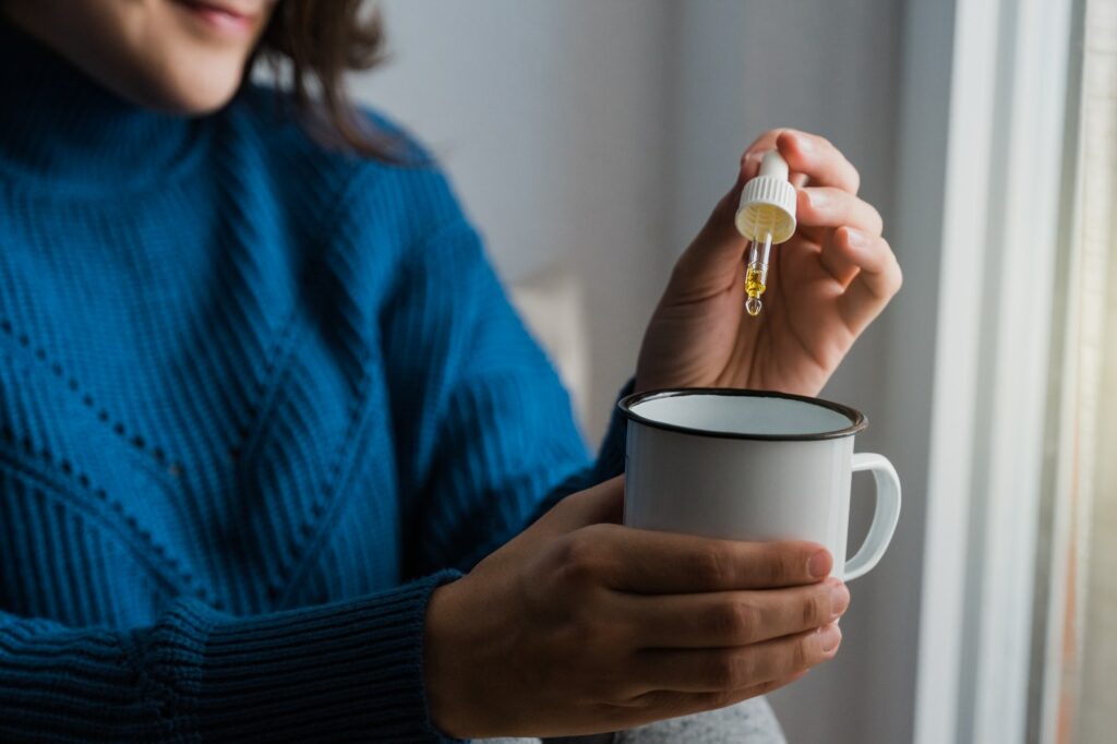 Woman taking Cannabis cbd oil inside tea cup - Alternative medicine, vitamins and supplements