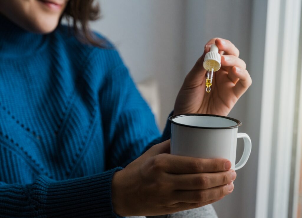 Woman taking Cannabis cbd oil inside tea cup - Alternative medicine, vitamins and supplements