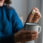 Woman taking Cannabis cbd oil inside tea cup - Alternative medicine, vitamins and supplements