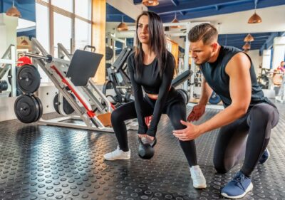 Personal trainer coaching female bodybuilder making plie squat with dumbbell