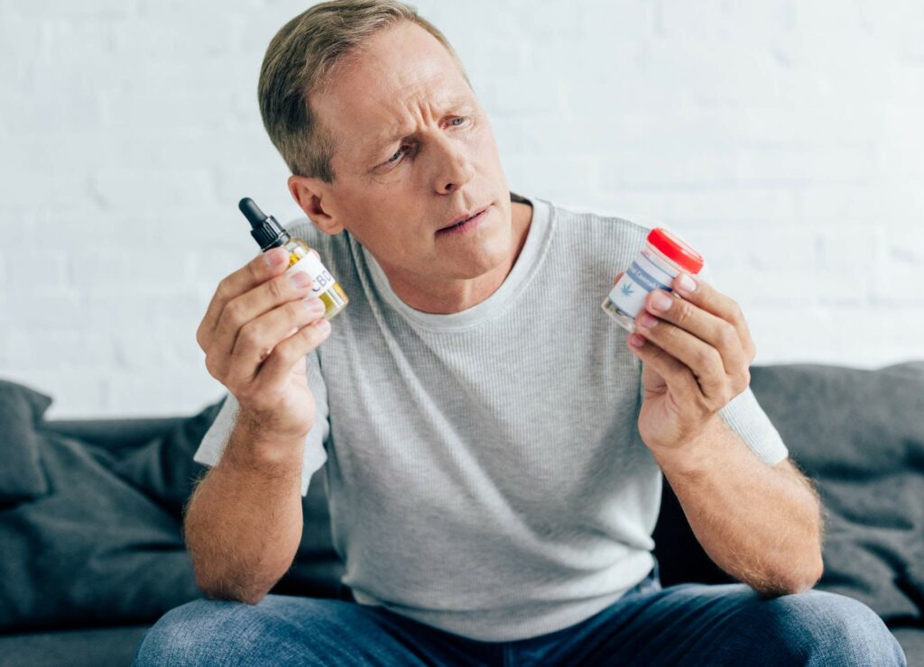 handsome man in t-shirt holding medical cannabis and cannabis oil